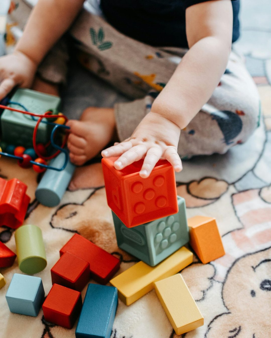 Toddler engaging with vibrant toy blocks on a patterned rug in a playful setting.